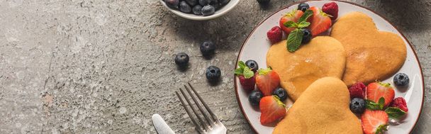 top view of heart shaped pancakes with berries on grey concrete surface with cutlery, panoramic shot - Photo, image