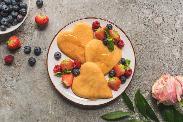 top view of heart shaped pancakes with berries on grey concrete surface near rose - Fotografie, Obrázek