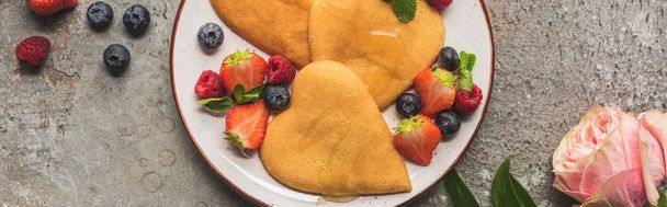 top view of heart shaped pancakes with berries on grey concrete surface near rose, panoramic shot - Photo, Image