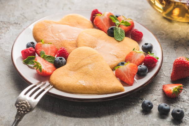 вкусные блинчики в форме сердца с ягодами на тарелке с вилкой на серой бетонной поверхности
 - Фото, изображение