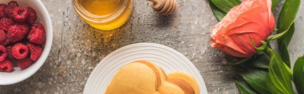 top view of heart shaped pancakes with berries, honey and rose on grey concrete surface, panoramic shot - 写真・画像