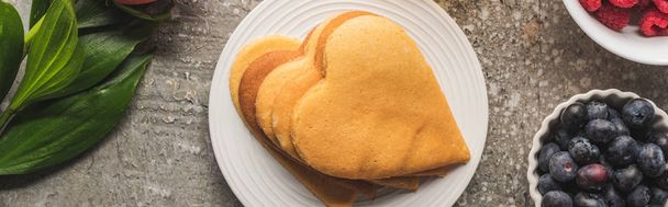 top view of heart shaped pancakes with berries and rose on grey concrete surface, panoramic shot - Foto, immagini