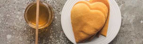 top view of heart shaped pancakes near honey on grey concrete surface, panoramic shot - Photo, Image