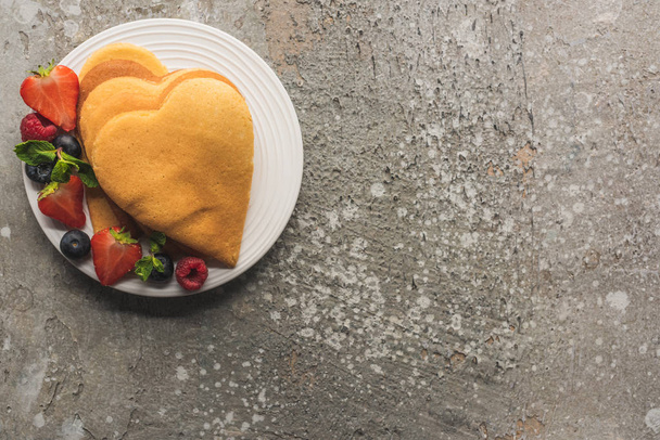 top view of heart shaped pancakes with berries on grey concrete surface - Photo, image