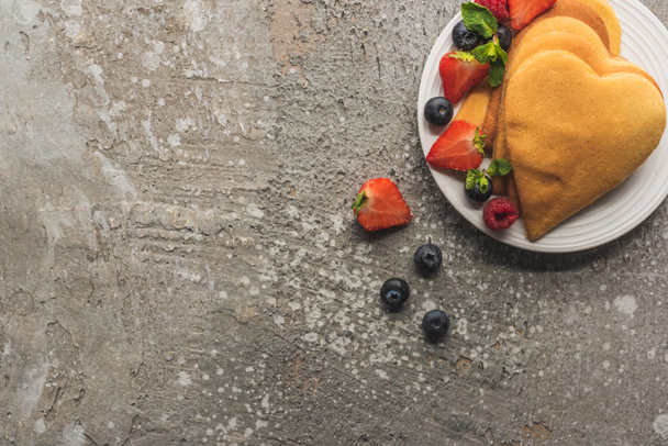 top view of heart shaped pancakes with tasty berries on plate on grey concrete surface - Foto, immagini
