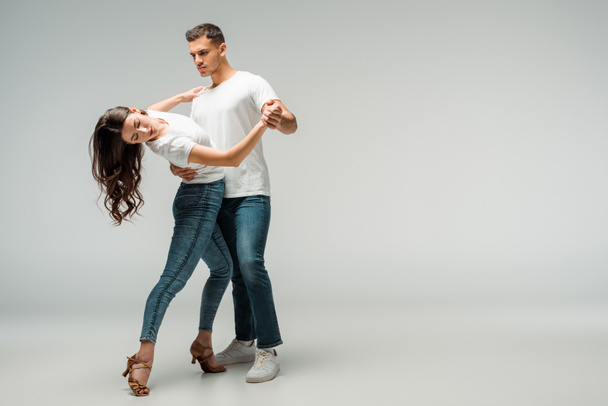Tänzer in T-Shirts und Jeans tanzen Bachata auf grauem Hintergrund  - Foto, Bild