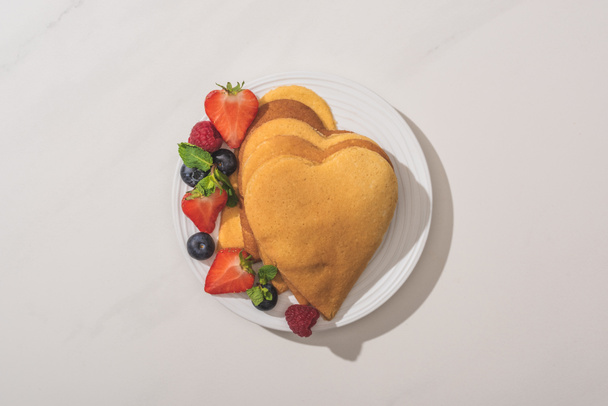 top view of heart shaped pancakes with tasty berries on plate on white background - Фото, изображение