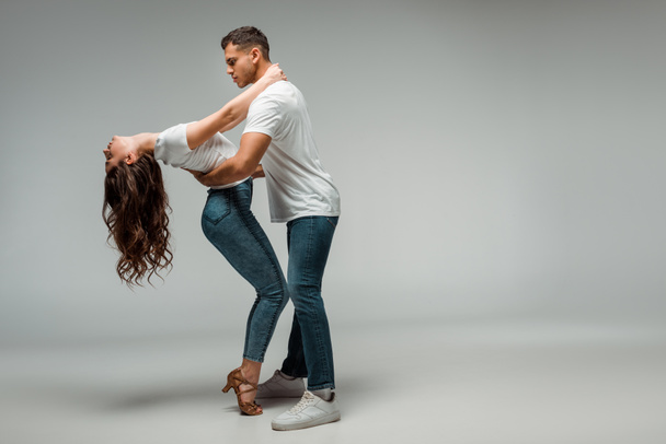 side view of dancers in t-shirts and jeans dancing bachata on grey background  - Photo, image