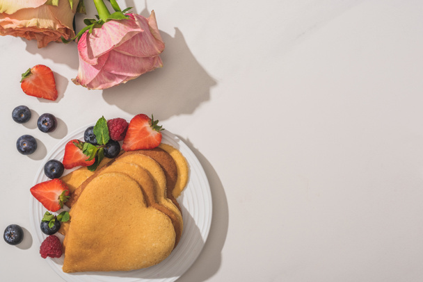 top view of delicious heart shaped pancakes with berries near roses on white background - Photo, image
