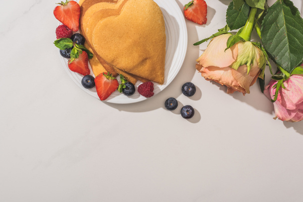 top view of delicious heart shaped pancakes with berries near roses on white background - Foto, immagini