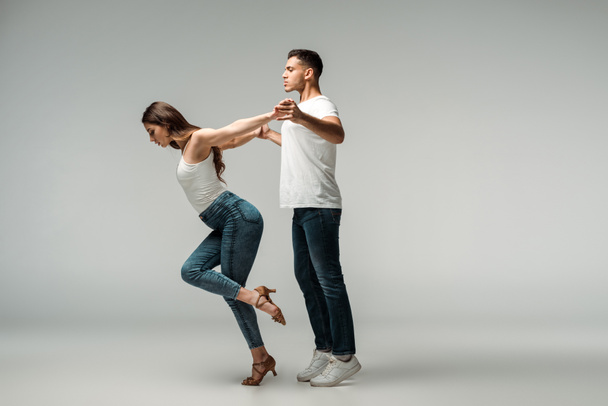 side view of dancers in denim jeans dancing bachata on grey background  - Photo, Image