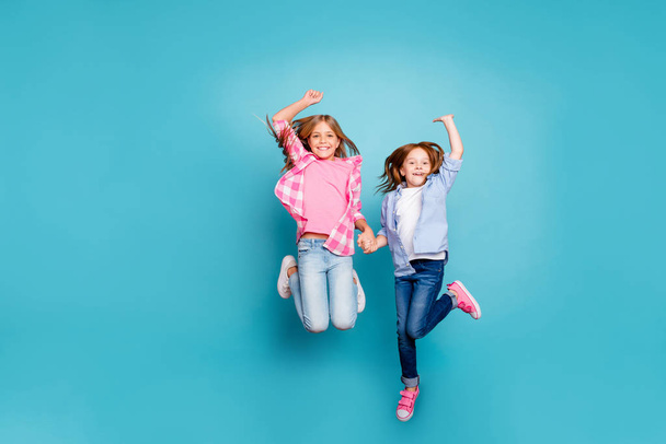 Full length body size photo of two rejoicing encouraged excited free girls jumping while isolated with blue background - Fotó, kép