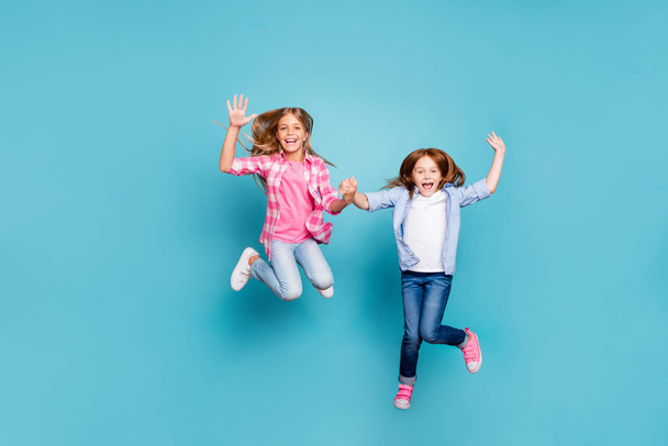 Full length body size photo of two excited cheerful overjoyed optimistic girls wearing jeans denim white while isolated with blue background - Фото, изображение