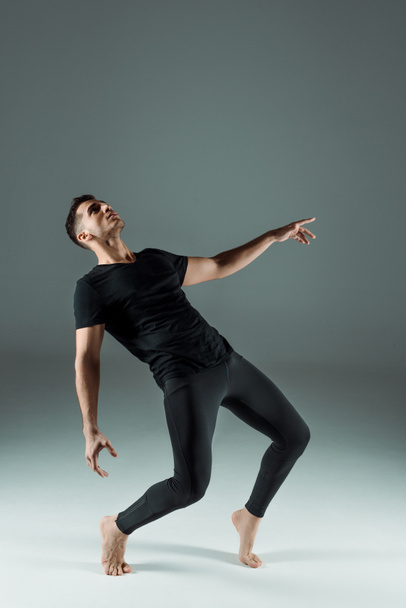 handsome dancer in black leggings and t-shirt dancing contemporary on dark background - Фото, изображение