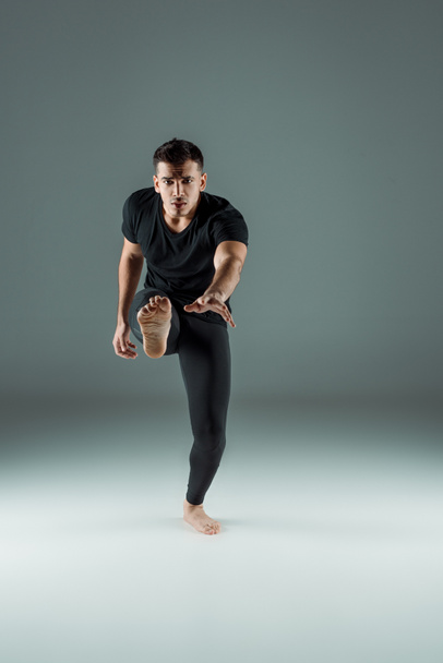 handsome dancer in black leggings and t-shirt dancing contemporary on dark background - Photo, Image