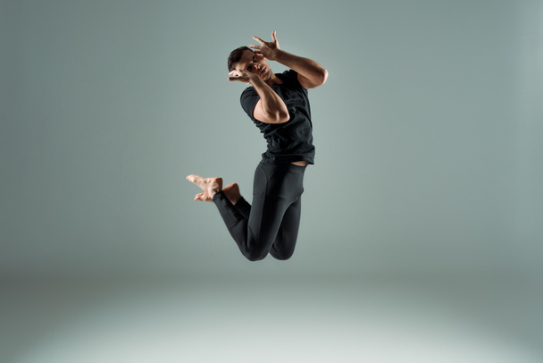 handsome dancer with closed eyes in black leggings and t-shirt dancing contemporary on dark background - Foto, Bild