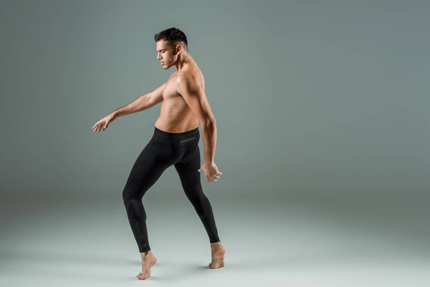 side view of handsome dancer in black leggings dancing contemporary on dark background - Fotografie, Obrázek