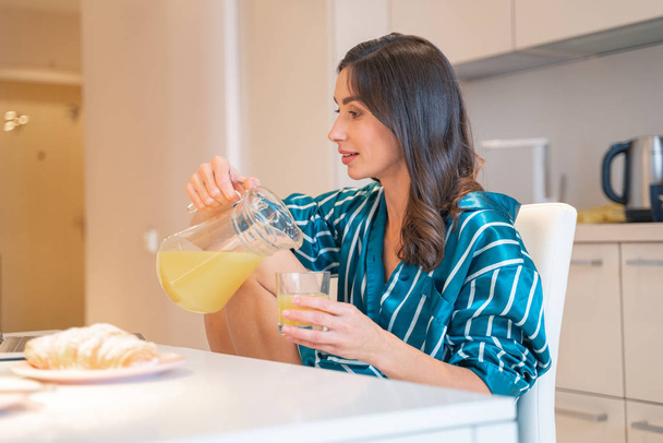 Calm woman pouring juice in the kitchen stock photo - Foto, Imagen