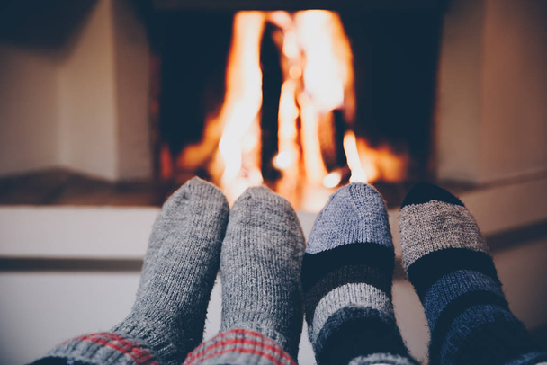 Feet in wool striped socks by the fireplace. Relaxing at Christmas fireplace on holiday evening. - Photo, Image