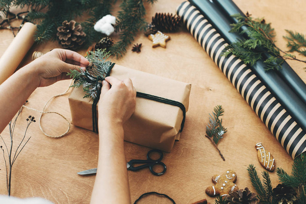 Руки обертывают деревенский рождественский подарок, завязывают зеленую веревку и булавку
 - Фото, изображение