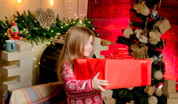Niña de Navidad con un gran regalo de Navidad en sus manos. Hermosa niña usando suéter rojo
. - Foto, imagen