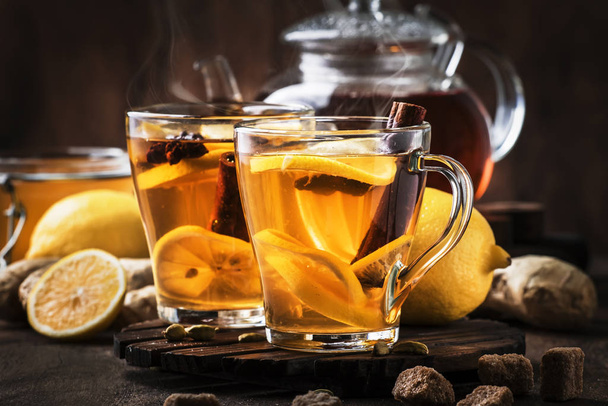 Χειμώνας ή φθινόπωρο ζεστό τσάι επούλωσης με τζίντζερ, μέλι, λεμόνι και μπαχαρικά σε γυάλινο κύπελλο με ατμό, ρουστίκ ξύλινο φόντο - Φωτογραφία, εικόνα