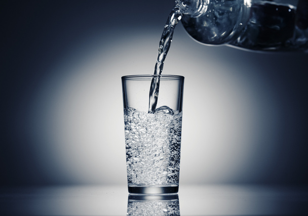 nalewanie wody gazowanej do szklanki na ciemnoniebieskim tle - Zdjęcie, obraz