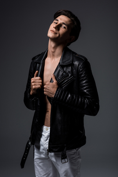 handsome sexy man in white jeans and black leather jacket, isolated on grey - Foto, afbeelding