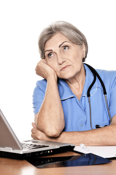 Serious elderly woman doctor sitting at table with computer  - Foto, Bild