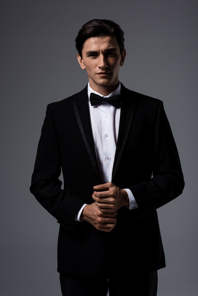 handsome young man in suit and tie bow, isolated on grey - Fotó, kép