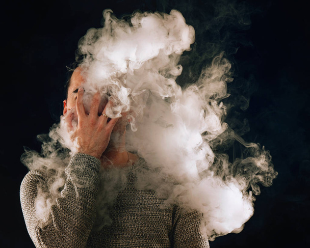 smoking man in e-cigarette smoke on black background - Фото, изображение