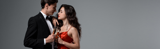 panoráma felvétel romantikus pár kezében pezsgős poharak és egymásra néz, elszigetelt szürke - Fotó, kép