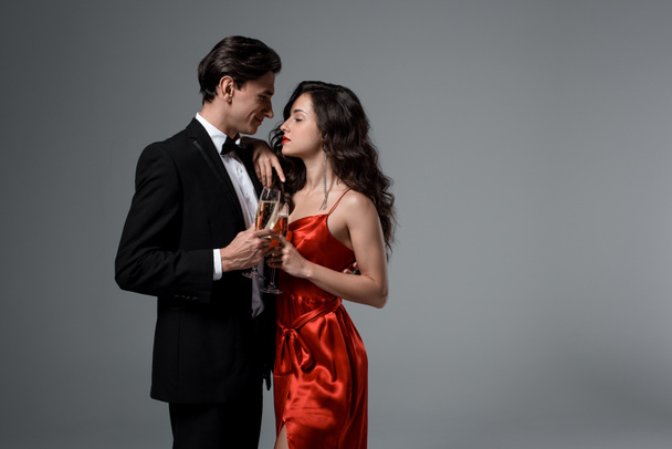 Paar hält Champagnergläser in der Hand, während es sich anschaut, isoliert auf grau - Foto, Bild