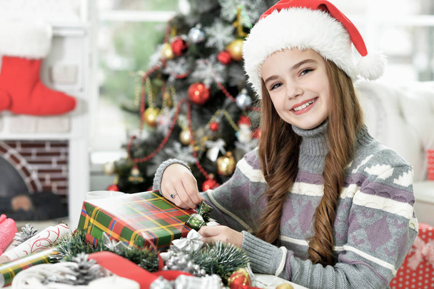 Portrait of happy girl in Santa hat sitting  with Christmas present - Fotó, kép