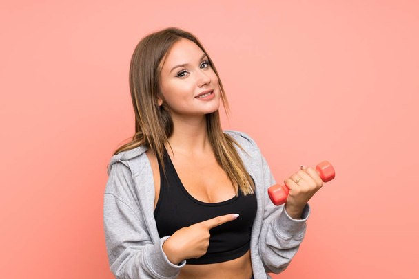 Teenager sport girl making weightlifting over isolated pink background and pointing it - Foto, afbeelding