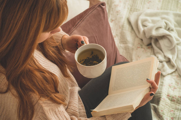 Femme buvant du thé chaud et lisant le livre. Développement et détente
 - Photo, image