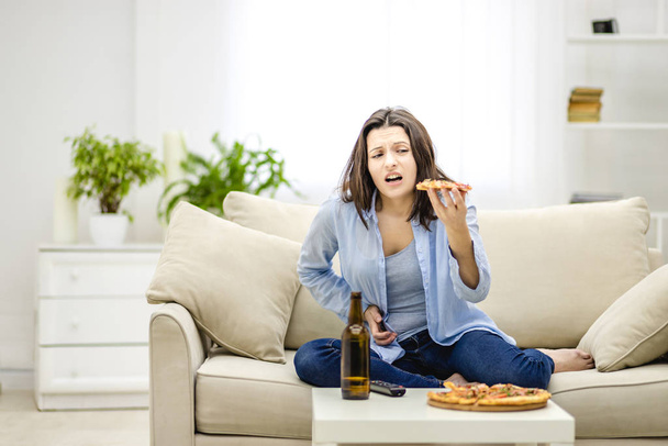 Brunette woman holds a slice of pizza. She feels stomachache. Woman overeaten at lot. Copy space. - Photo, Image