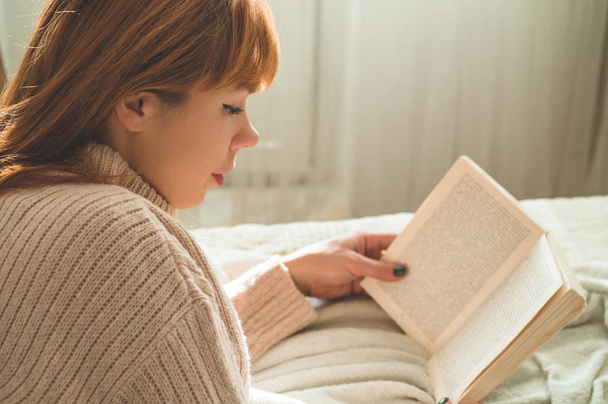 Viehättävä nuori nainen lukee kirjaa kotona. Ajattelevainen tyttö käsittelyssä tärkeä kirja
. - Valokuva, kuva