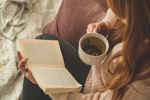 Een vrouw die hete thee drinkt en een boek leest. Ontwikkeling en ontspanning - Foto, afbeelding