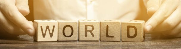 A man puts wooden blocks with the word World. The concept of globalization and global business. International relationships. Diplomacy. Investments and economics. Geography - Photo, Image