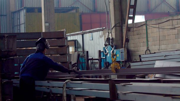 Trabalhador com um guindaste levanta um perfil de metal longo
 - Foto, Imagem