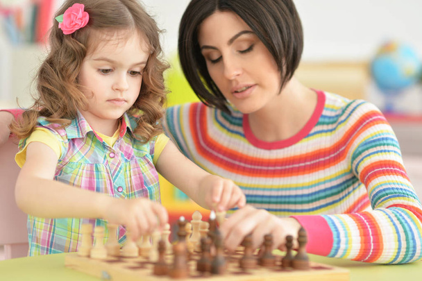 Beautiful young mother with her cute little daughter playing chess  - Φωτογραφία, εικόνα
