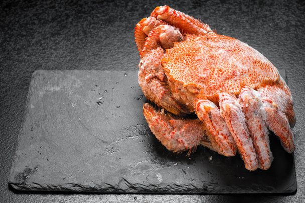 Icy hairy crab laying on the black table and slate board, side view. - Photo, Image