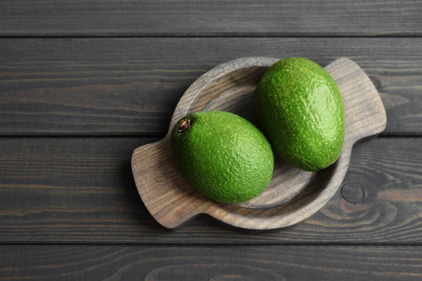 Fresh organic avocado in wooden plate over dark wooden table background - Photo, image