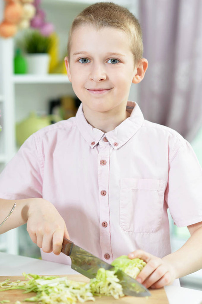 Cute boy preparing salad on kitchen table at home - Valokuva, kuva