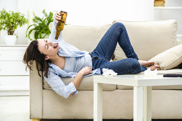 Drunk woman is laying on the sofa and looking at the empty bottle of beer. - Foto, Imagem
