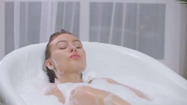 Mooie vrouw ontspannen in bubbelbad liggend in bad. vrolijk en ontspannen liggend in bad met schuimbellen bad thuis of hotel badkamer lachend speels genietend van luxe levensstijl - Video