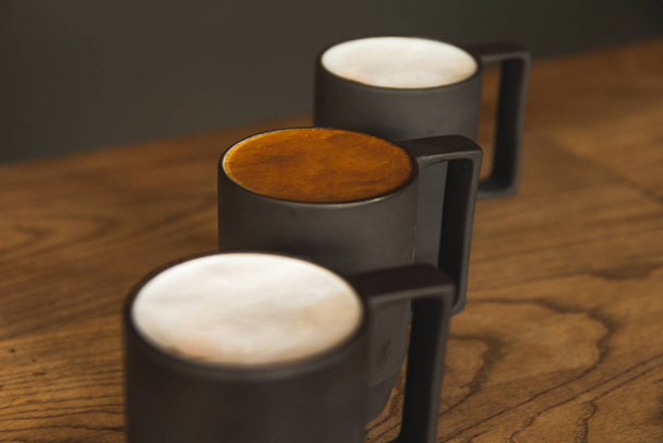 Τρία ποτήρια καφέ λάτε σε ξύλινο τραπέζι με λευκό και καφέ αφρό - Φωτογραφία, εικόνα