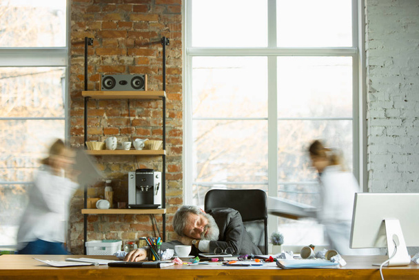 Tired boss resting at his workplace while people moving near blurred - Foto, imagen