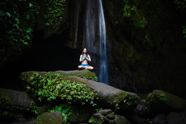 Молода кавказька жінка медитує, практикуючи йогу при водоспаді. Руки в ім'я мудра. Водоспад Leke Leke, Балі, Індонезія.  - Фото, зображення